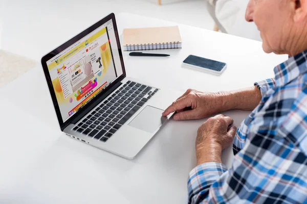 Teilansicht eines älteren Mannes, der am Tisch sitzt und Laptop mit aliexpress-Logo benutzt — Stockfoto