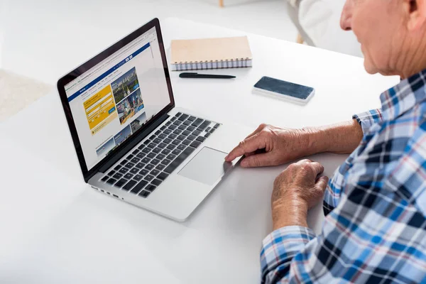 Visão parcial do homem sênior sentado à mesa e usando laptop com logotipo com reserva — Fotografia de Stock