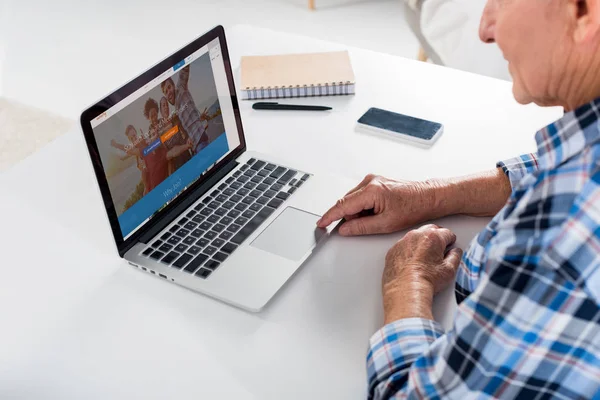 Partial view of senior man working on laptop at table with notebook at home — Stock Photo