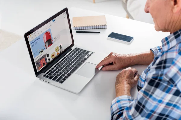 Teilansicht eines älteren Mannes, der zu Hause am Laptop mit ebay-Logo am Tisch mit Notebook arbeitet — Stockfoto