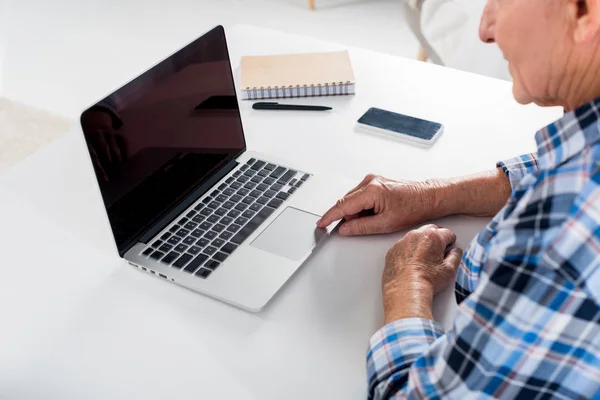 Vue partielle de l'homme âgé travaillant sur un ordinateur portable avec écran vierge à la table avec ordinateur portable à la maison — Photo de stock