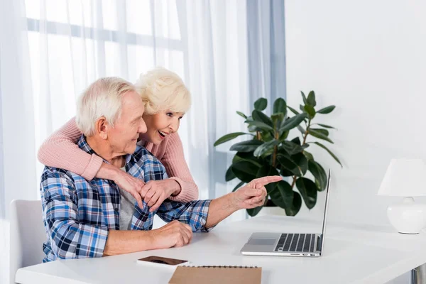 Side view of happy senior couple using laptop together at home — Stock Photo