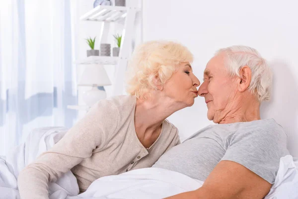 Seniorin küsst Mann, während sie morgens zu Hause zusammen im Bett liegt — Stockfoto