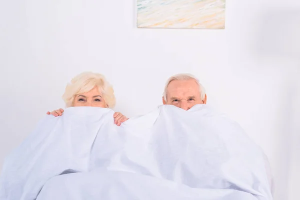 Vista oscurecida de la esposa mayor y el marido cubriendo caras con manta y mirando a la cámara - foto de stock