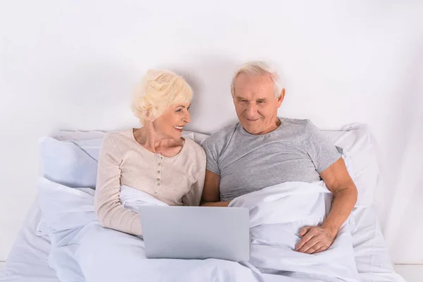 Couple âgé utilisant un ordinateur portable tout en se reposant dans le lit à la maison — Photo de stock