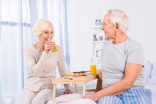 Счастливая пожилая пара, завтракающая вместе в постели дома — стоковое фото