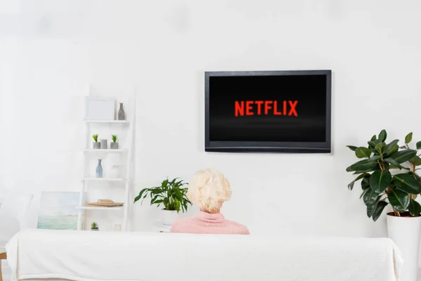 Пожилая женщина смотрит телевизор с логотипом netflix на экране — стоковое фото