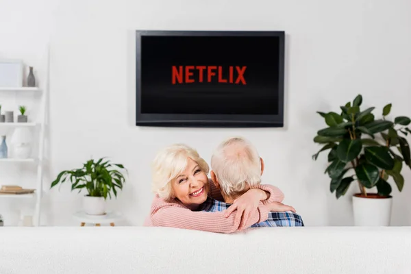 Seniorenpaar umarmt sich auf Couch vor dem Fernseher mit Netflix-Logo auf dem Bildschirm — Stockfoto