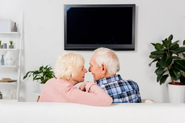 Senior couple sitting on couch in front of tv at home — Stock Photo