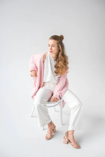 Belle fille avec de longs cheveux bouclés assis sur la chaise et regardant loin sur blanc — Photo de stock