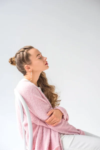 Hermosa chica en camisa rosa sentado en silla de madera con los ojos cerrados aislados en blanco - foto de stock