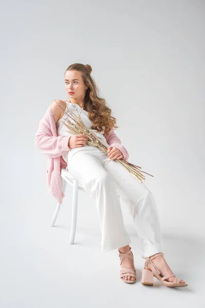 Schöne Frau sitzt auf Stuhl mit Weidenzweigen und Stacheln auf weißem Grund — Stockfoto