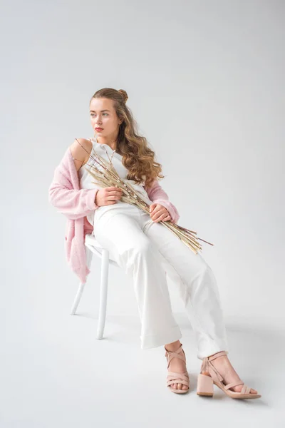 Belle femme assise sur une chaise avec des branches de saule et des épillets sur blanc — Photo de stock