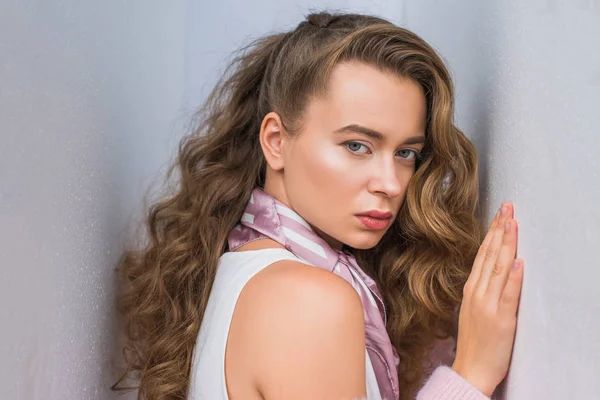 Attractive girl with curly hair leaning on gray wall and posing for fashion shoot — Stock Photo