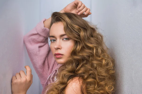 Fashionable woman with curly hair posing for fashion shoot between gray walls — Stock Photo