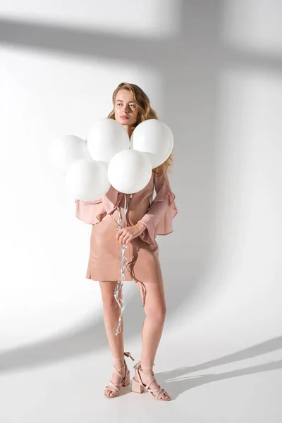 Attraktive Frau in beigem Kleid mit Bündel weißer Luftballons und wegschauendem Blick — Stockfoto