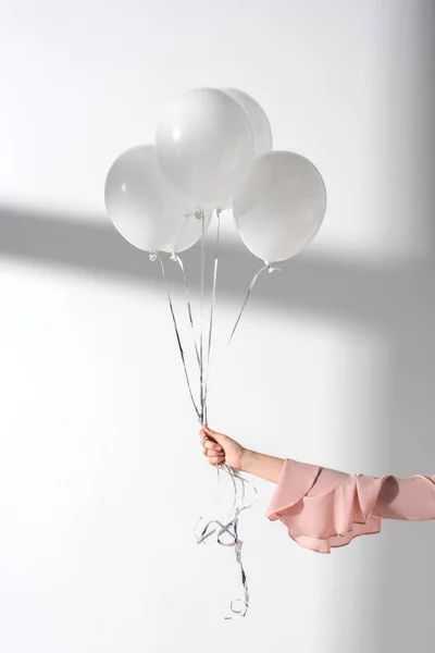 Imagen recortada de niña sosteniendo manojo de globos con helio en la mano - foto de stock