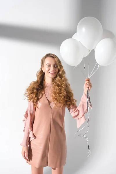 Happy girl in beige dress holding bundle of balloons with helium — Stock Photo