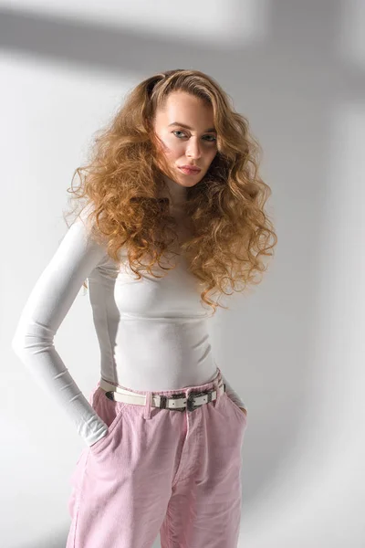 Chica con estilo de confianza con el pelo rizado de pie con las manos en los bolsillos y mirando a la cámara - foto de stock