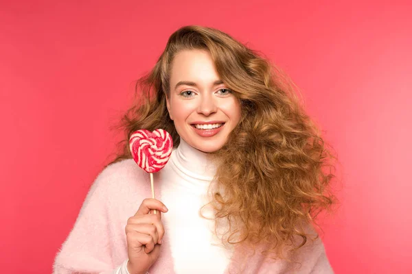 Happy woman standing with heart shaped lollipop and looking at camera isolated on red — Stock Photo