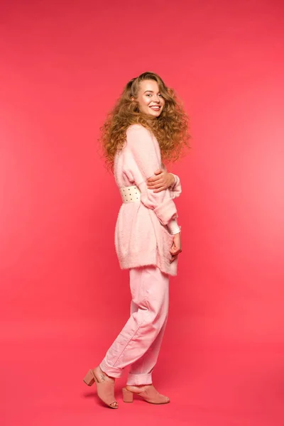 Stylish smiling girl standing in pink clothes and looking at camera isolated on red — Stock Photo