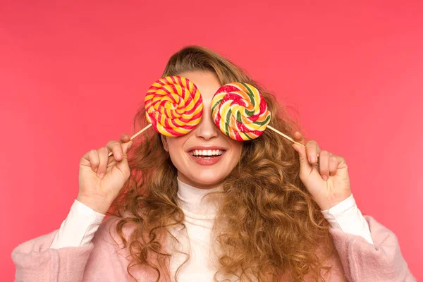 Menina feliz cobrindo os olhos com pirulitos redondos isolados no vermelho — Fotografia de Stock