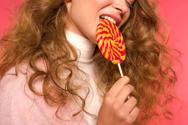 Imagen recortada de hermosa mujer mordiendo piruleta en rojo - foto de stock