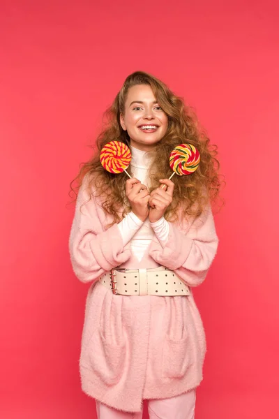 Happy stylish girl standing with two lollipops and looking at camera isolated on red — Stock Photo