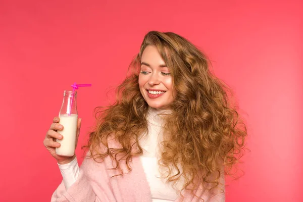 Menina sorrindo olhando para garrafa com milkshake e palha de plástico isolado no vermelho — Fotografia de Stock