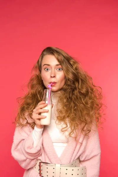Surprised girl drinking milkshake with plastic straw isolated on red — Stock Photo