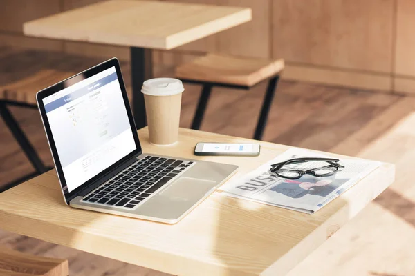 Laptop, Smartphone mit Facebook-Messenger und Wirtschaftszeitung auf dem Tisch im Café — Stockfoto
