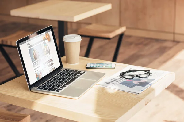Ноутбук, смартфон и деловая газета на столе в кафе — стоковое фото