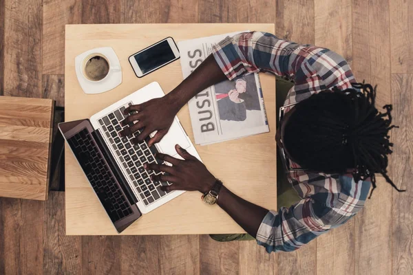 Vista aerea dell'uomo afroamericano con laptop, smartphone, tazza di caffè e giornale d'affari nel caffè — Foto stock
