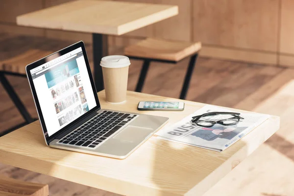 Ноутбук с веб-сайтом Amazon, смартфон и бизнес-газета на столе в кафе — стоковое фото