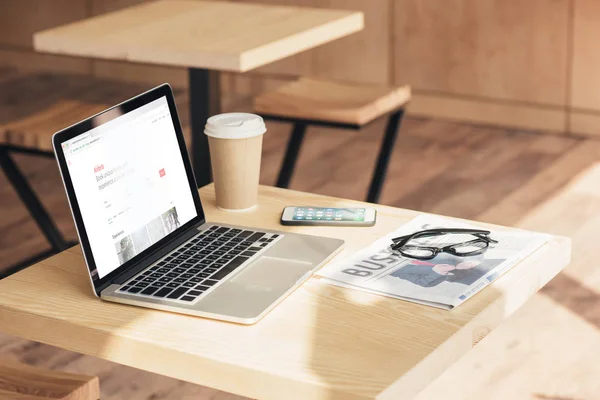 Portátil con sitio web airbnb, smartphone y periódico de negocios en la mesa en la cafetería - foto de stock