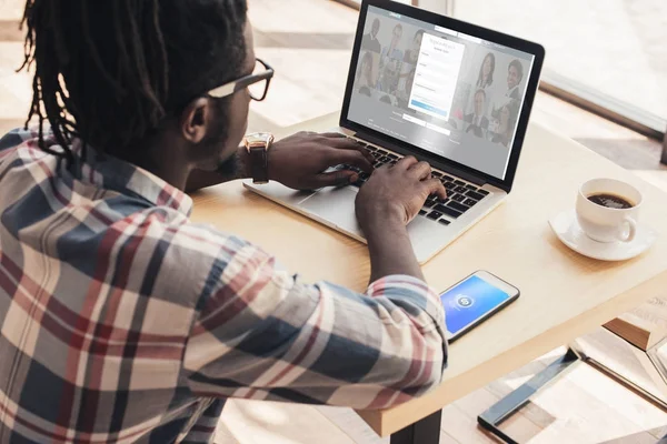 Афроамериканець людиною, використовуючи ноутбук з linkedin сайт і смартфон з shazam побутової техніки — стокове фото