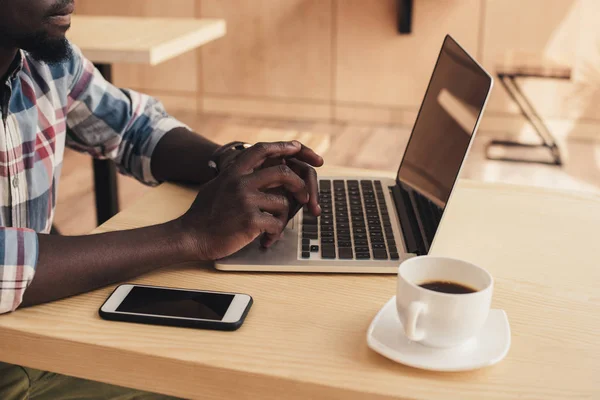 Vue recadrée de l'homme afro-américain à l'aide d'un ordinateur portable avec écran blanc dans le café — Photo de stock