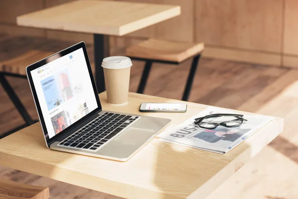 Laptop com site ebay, smartphone e jornal de negócios na mesa no café — Fotografia de Stock