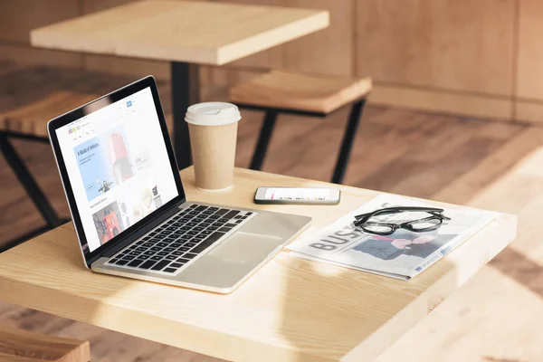 Laptop with ebay website, smartphone and business newspaper on table in coffee shop — Stock Photo