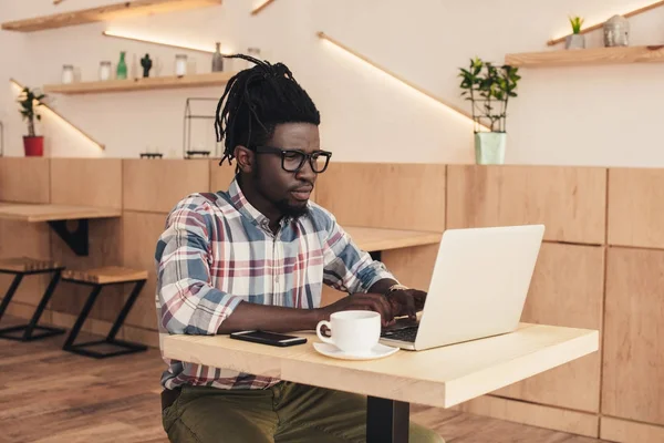 Homem americano africano usando laptop e smartphone no café — Fotografia de Stock