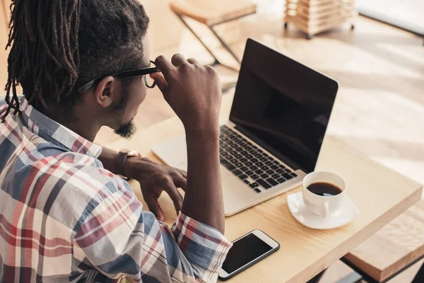 Uomo afroamericano utilizzando laptop e smartphone con schermi vuoti in caffetteria — Foto stock