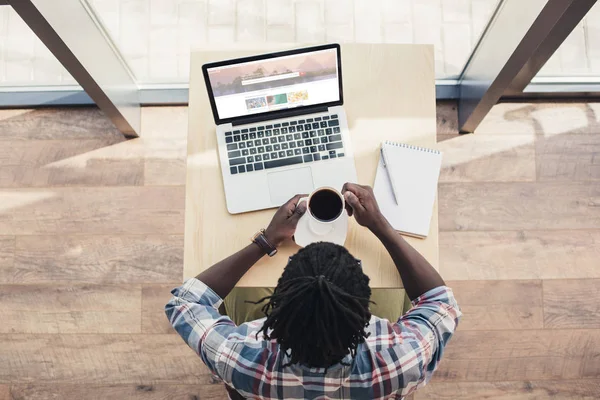 Overhead view of african american man drinking coffee and using laptop with shutterstock website — Stock Photo