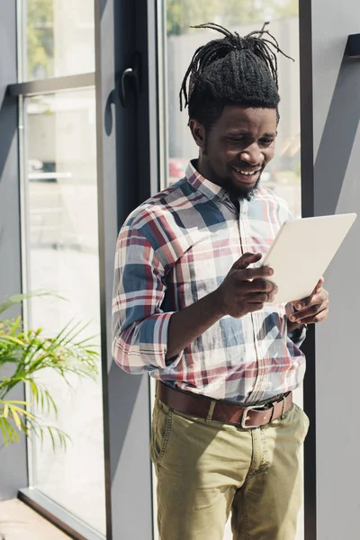 Uomo afroamericano utilizzando tablet digitale mentre in piedi alla finestra — Foto stock