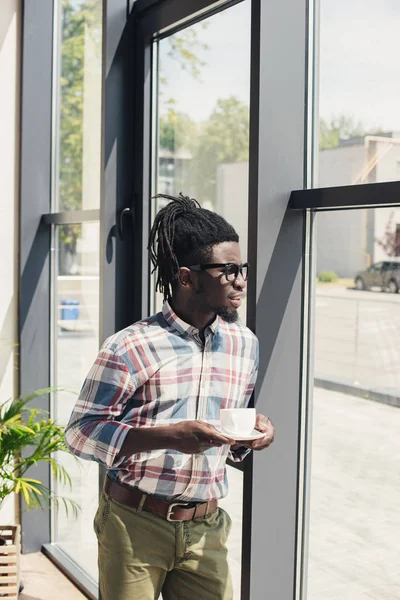 Africano americano uomo bere caffè mentre in piedi alla finestra — Foto stock