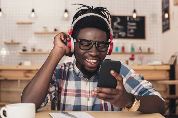 Homme afro-américain écouter de la musique et utiliser un smartphone dans un café — Photo de stock