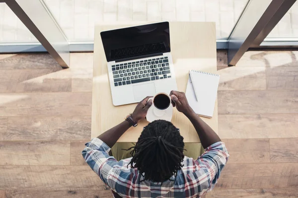 Vista aerea dell'uomo afro-americano che beve caffè e utilizza il computer portatile nel caffè — Foto stock