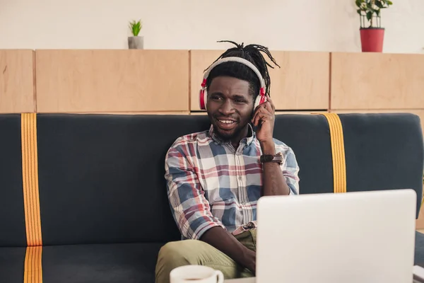 African american man listening music with headphones in coffee shop with laptop — Stock Photo