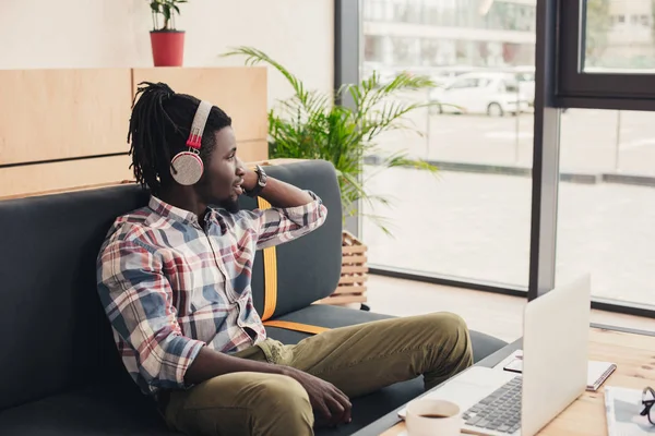 African american man listening music with headphones in coffee shop with laptop — Stock Photo