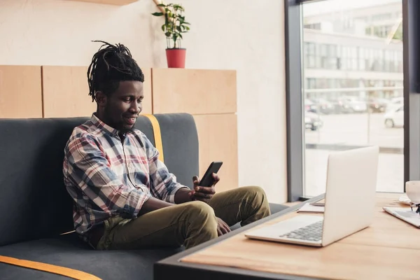 Африканский американец, использующий смартфон и ноутбук в кафе — стоковое фото
