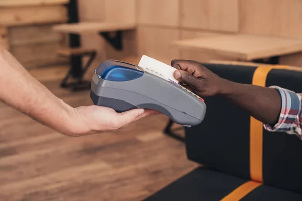 Cropped view of client paying with credit card and terminal in cafe — Stock Photo